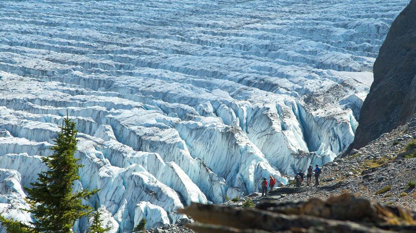 two hikers standing beside a massive blue glacier during a cmh heli-skiing and summer adventures guided tour in the canadian rockies