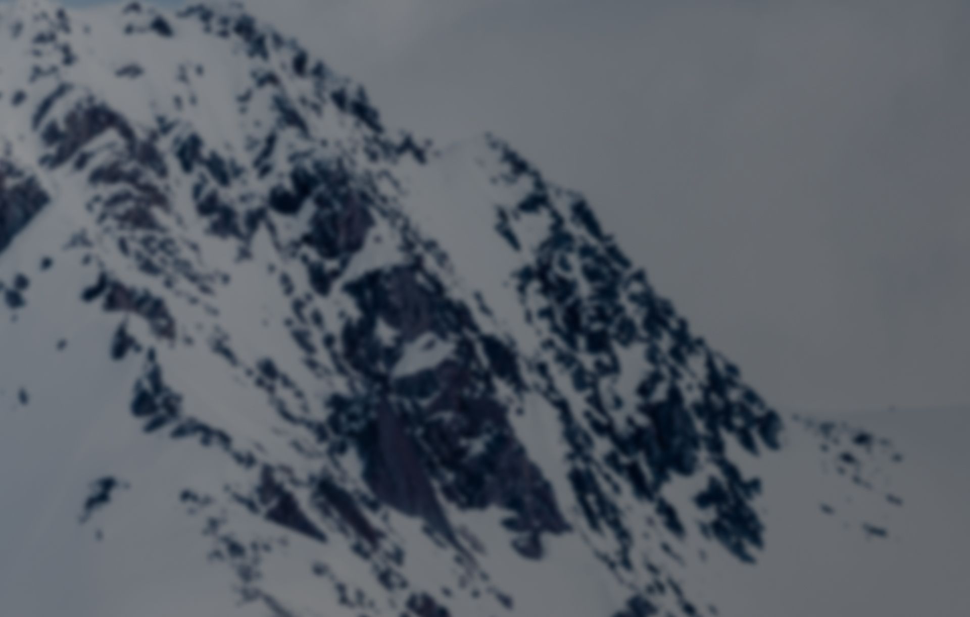 dramatic alpine peak covered in snow with rugged rock formations under overcast skies during a cmh heli-skiing mountain adventure