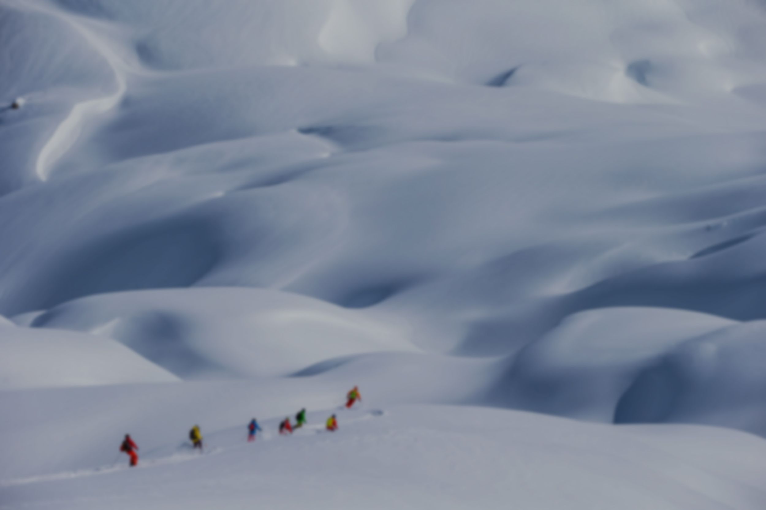 a group of skiers wearing bright jackets are seen in the distance of a dramatic snow covered landscape.
