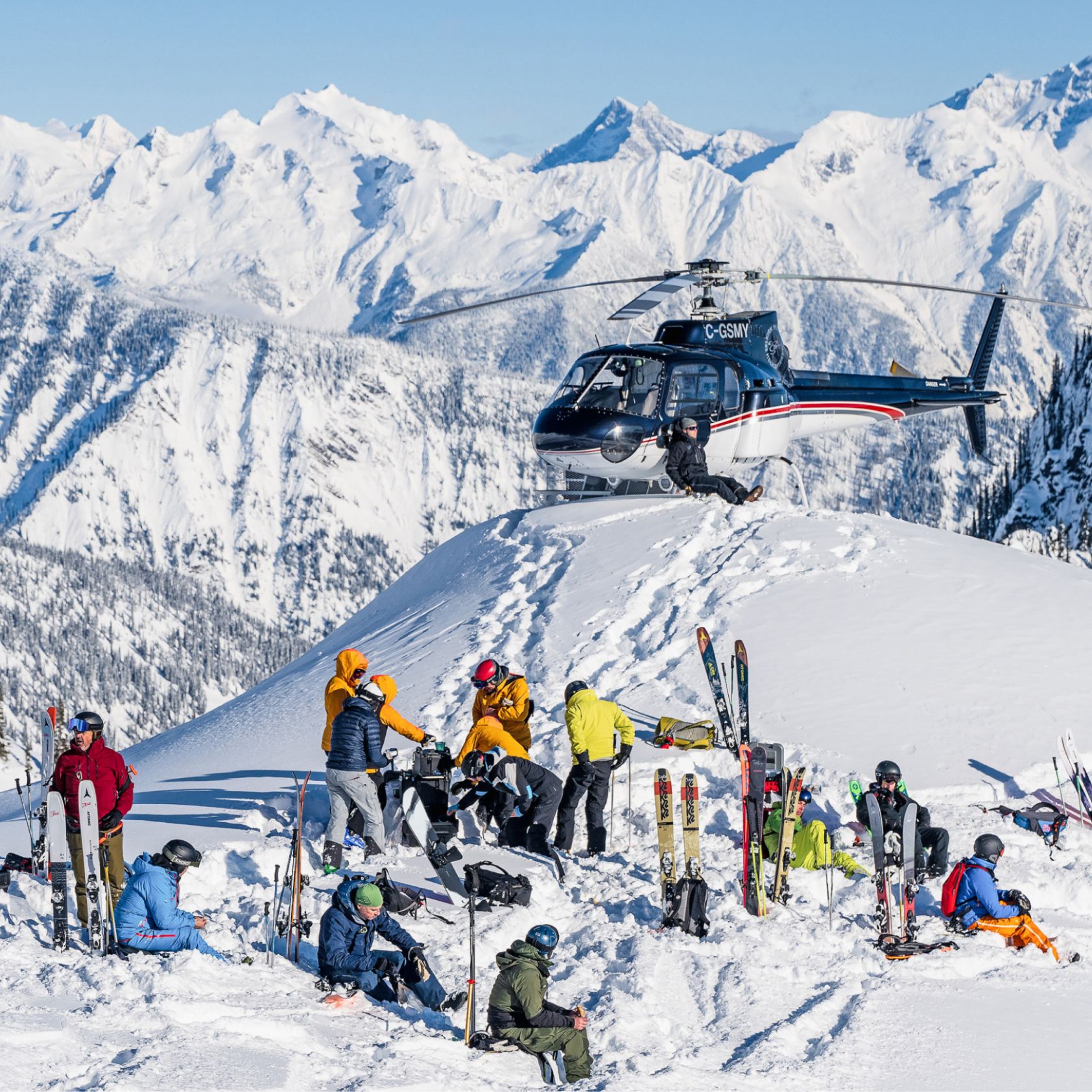 Skiers and riders getting ready at the top of the mountain. A helicopter is seen in the background.