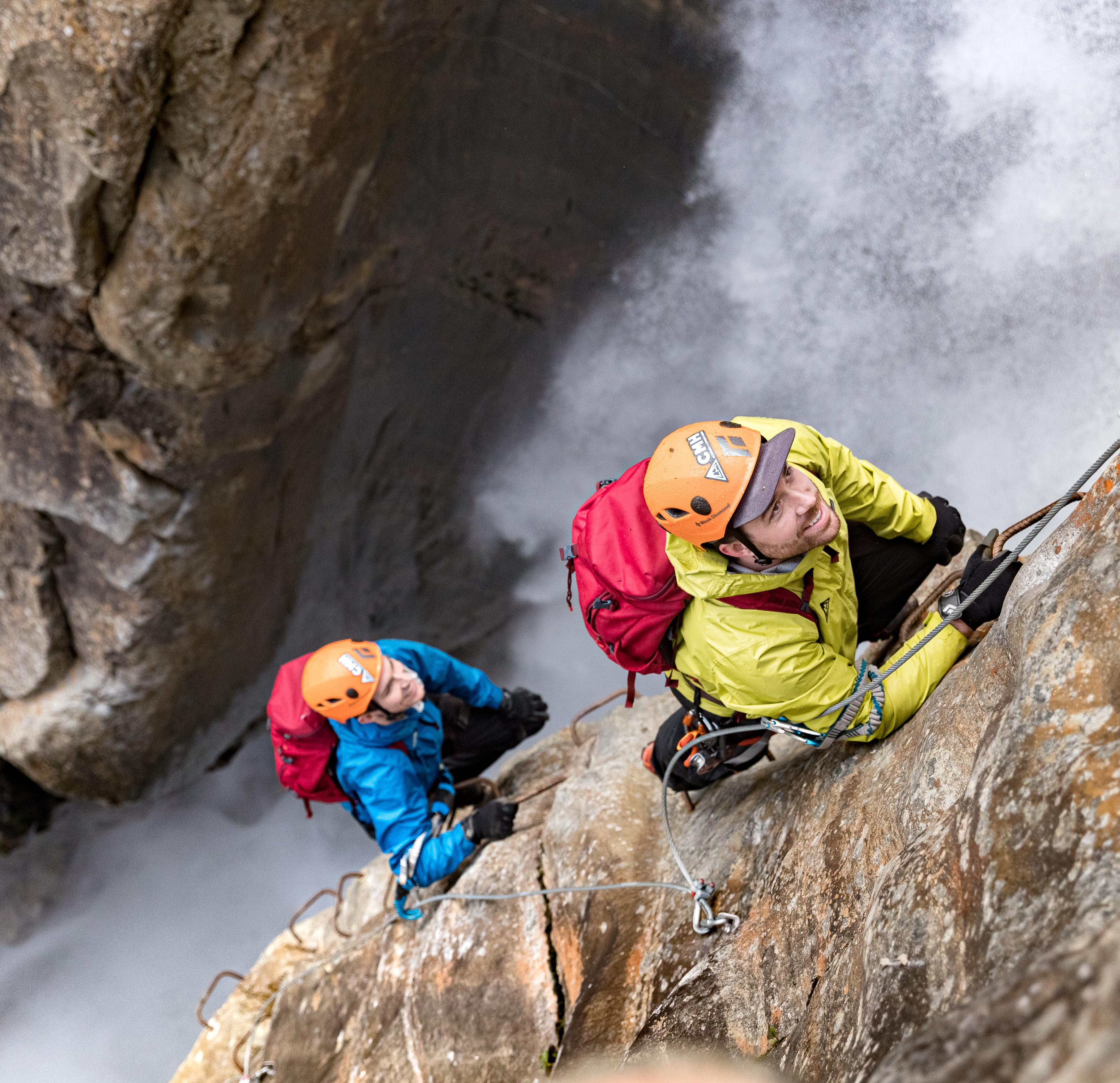 Two people climbing alongside a waterfall