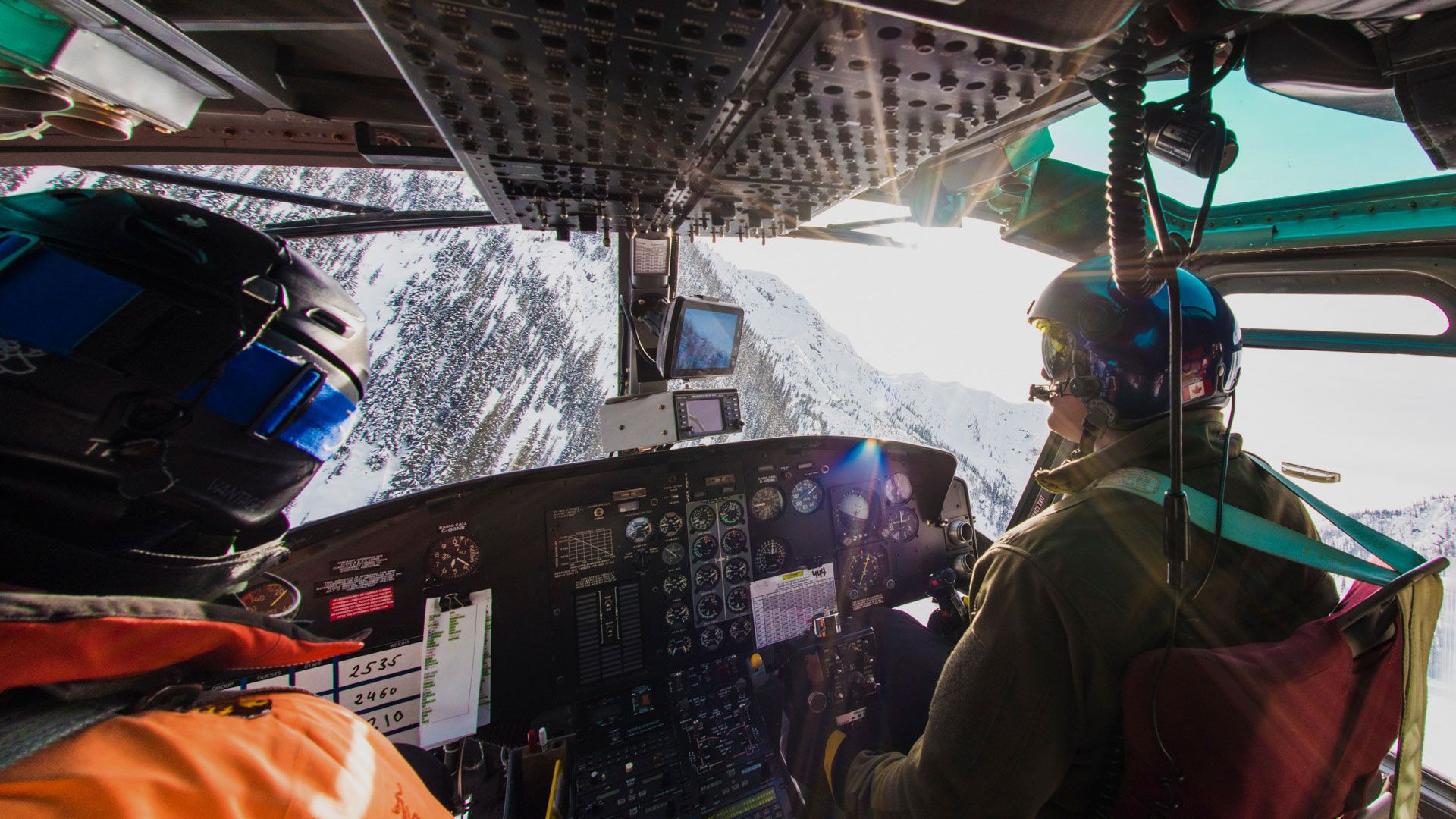 view from the cockpit of the helicopter showing the pilot and the sunlit snowy mountains capturing the thrilling flight experience of cmh heli-skiing