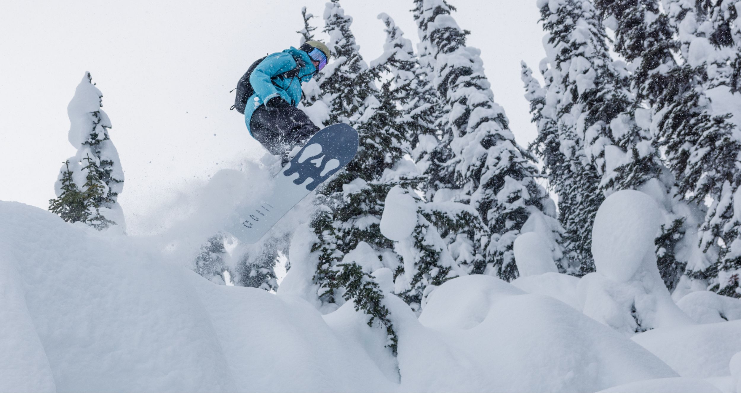 snowboarder in a blue winter jacket in mid air going off a snow bank