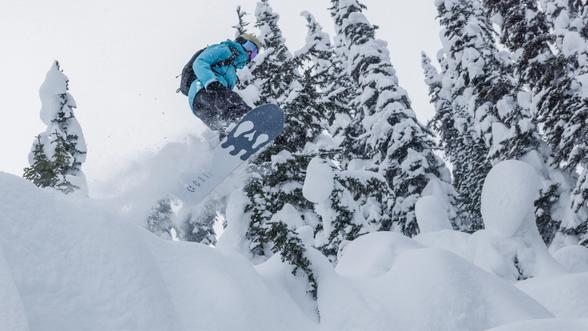 snowboarder in a blue winter jacket in mid air going off a snow bank