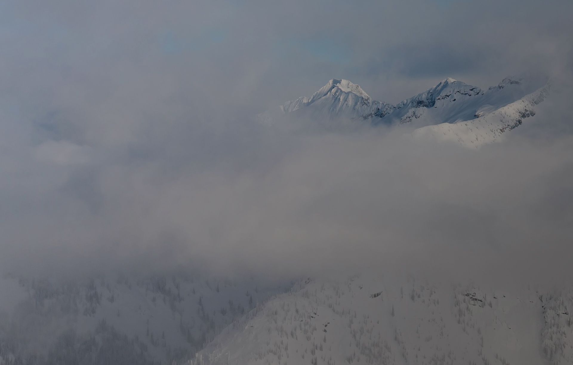 Snow-covered mountain peaks partially hidden by thick clouds and mist.