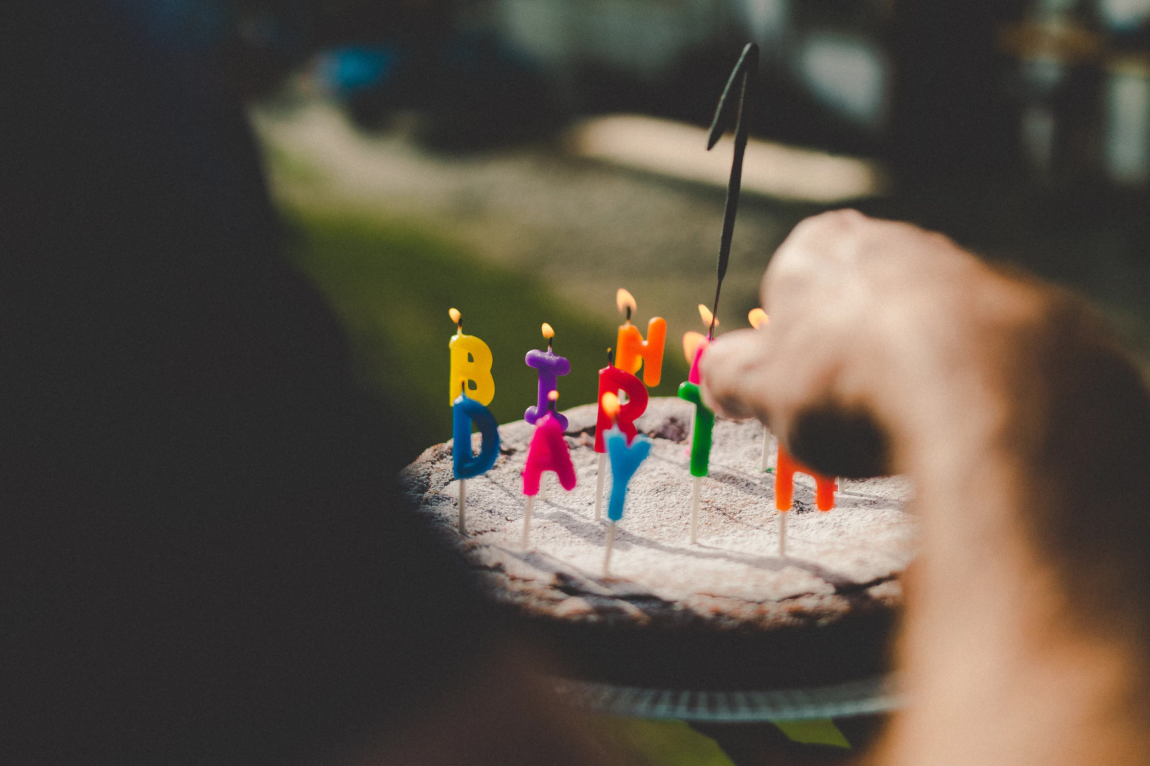 A hand lighting a candle on a cake decorated with letter candles spelling out Happy Birthday