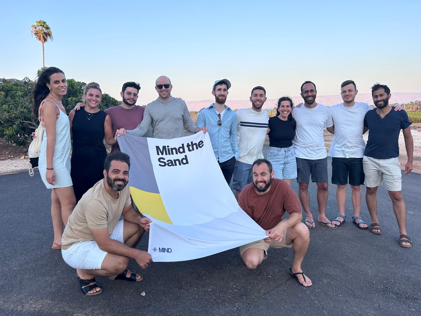 MIND team on the beach with a "Mind the Sand" towel
