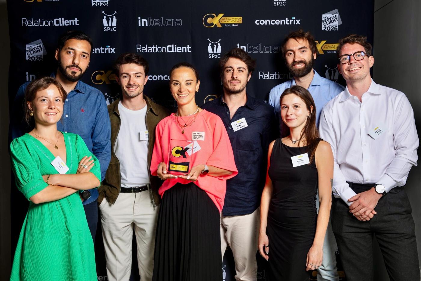 Seven members of the AlloBrain team holding the gold trophy in front of the CX Awards press wall