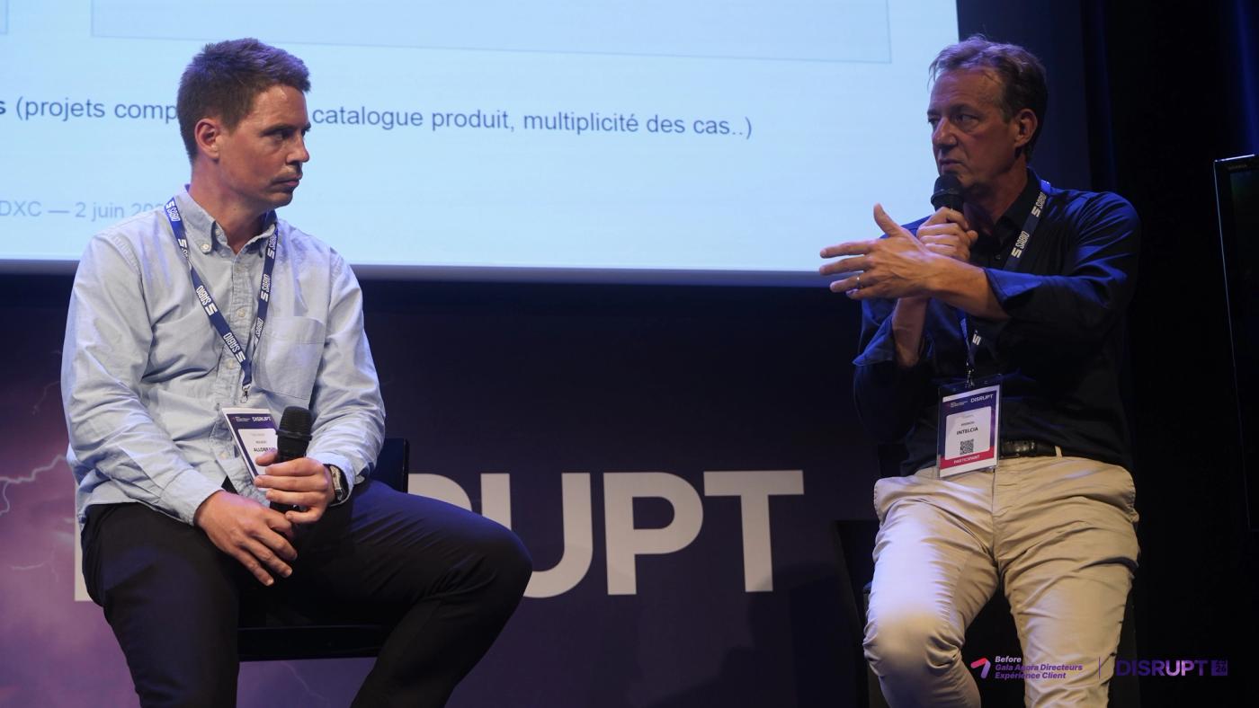 Two speakers in conversation on stage, a presentation slide projected behind them