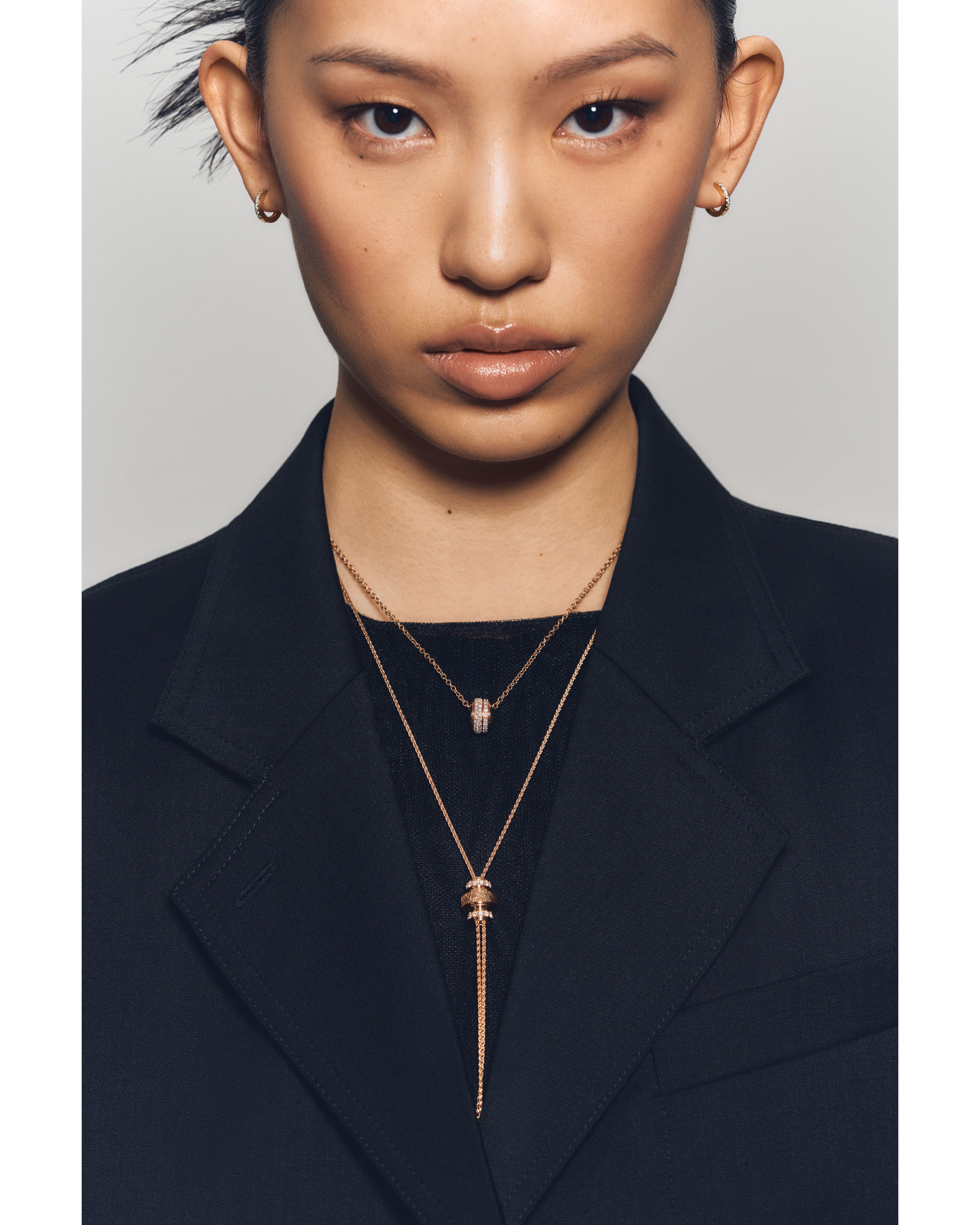 Front-facing portrait of a woman wearing a dark blazer, styled with minimalist gold hoop earrings and layered rose gold necklaces from the Piaget Possession collection, featuring pavé diamond accents.