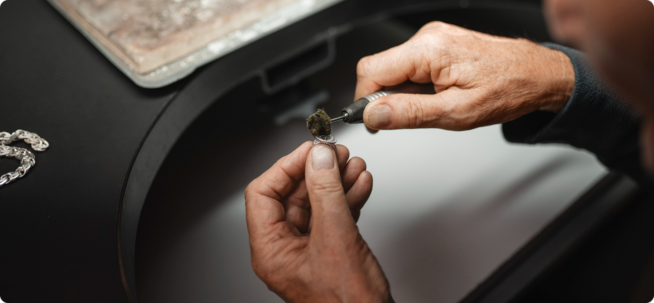 Plan rapproché des mains d'un joaillier polissant méticuleusement une bague en diamant dans un atelier, démontrant une qualité artisanale faite à la main.