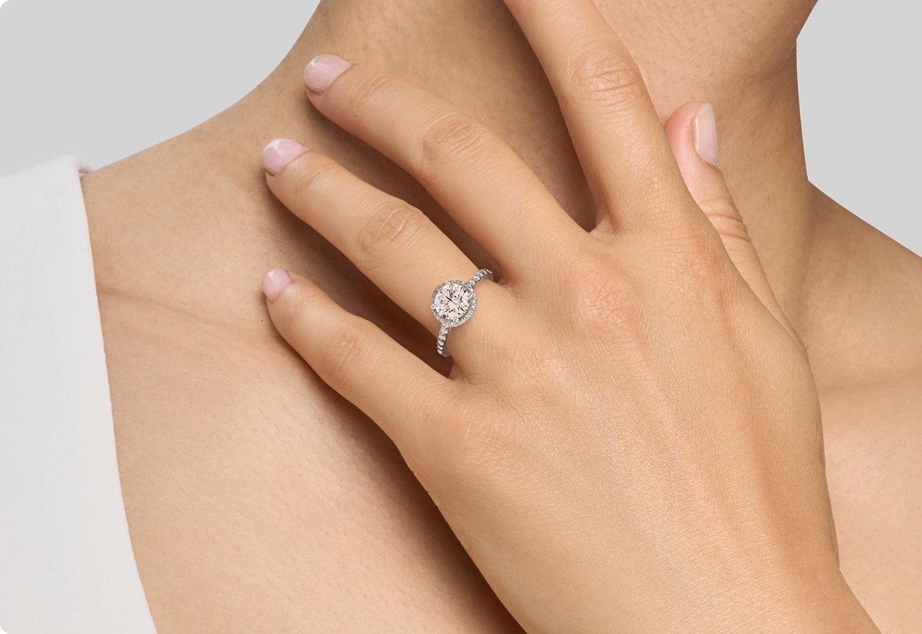 Plan rapproché d'une femme portant une bague de fiançailles étincelante en diamant L'Amour Uni au doigt, présentée sur un fond neutre.
