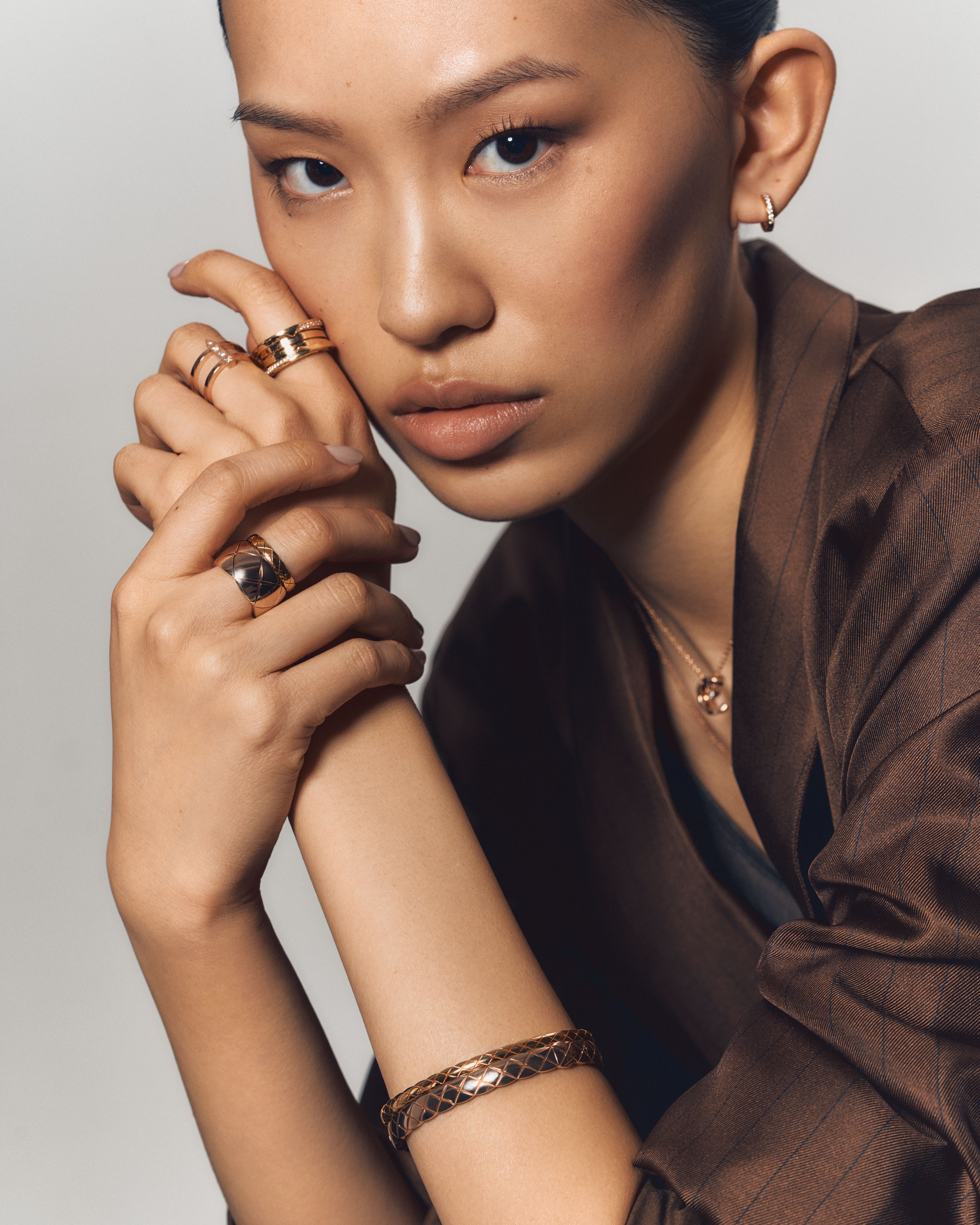 Close-up of a woman wearing stacked gold rings, a quilted-pattern gold bracelet, and a pendant necklace, showcasing the Chanel Coco Crush collection.