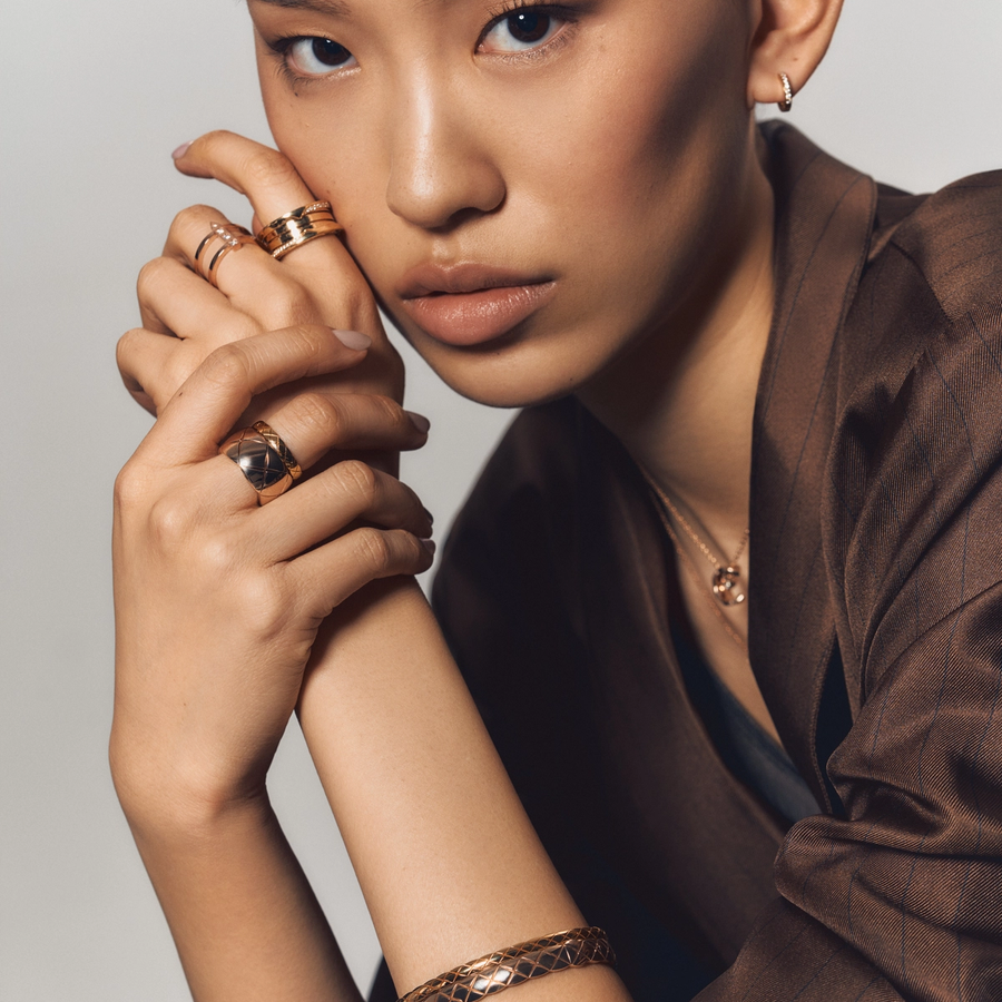 Close-up of a woman wearing stacked gold rings, a quilted-pattern gold bracelet, and a pendant necklace, showcasing the Chanel Coco Crush collection.
