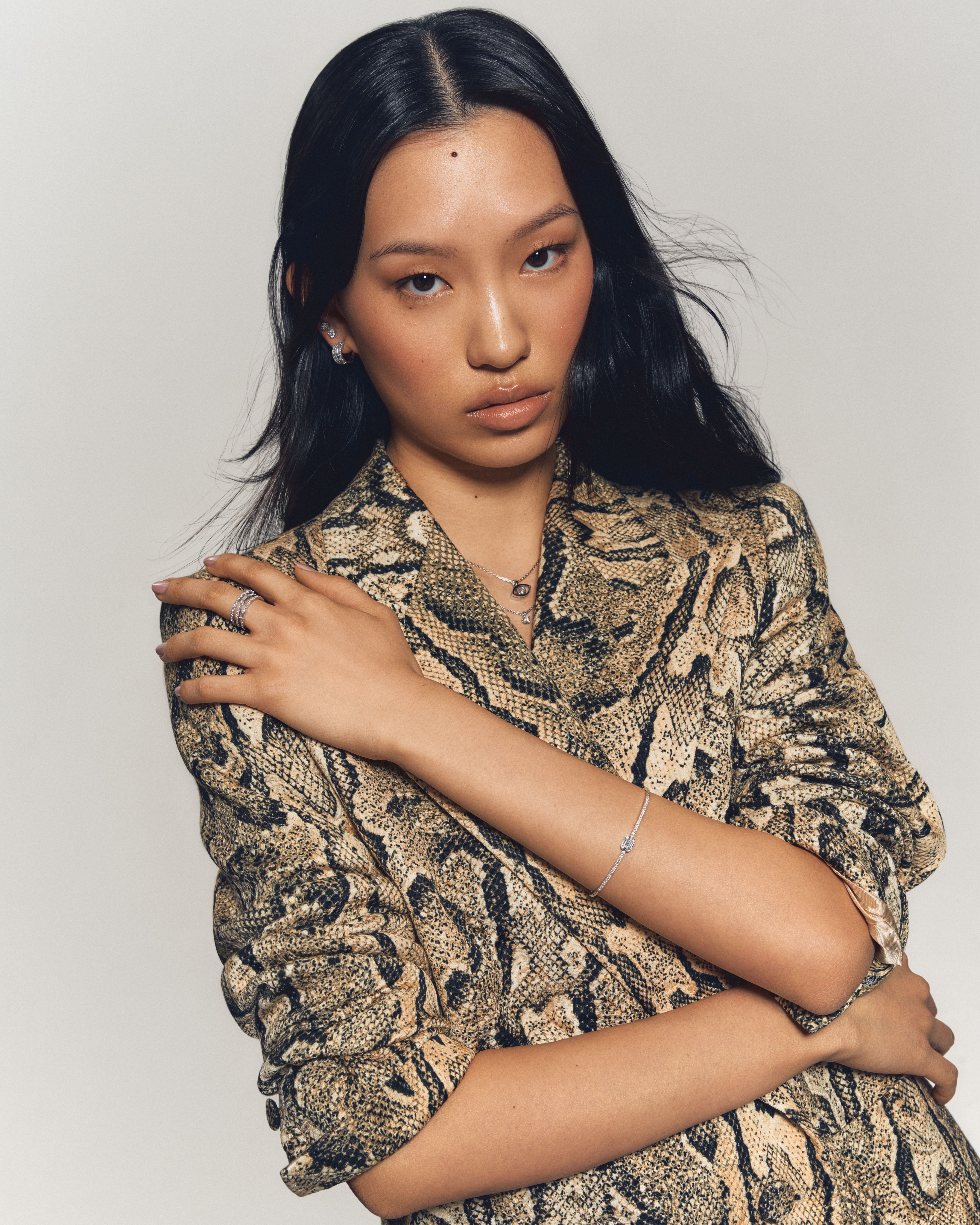  Portrait of a woman wearing a snakeskin-patterned blazer, styled with diamond earrings, a delicate pavé bracelet, stacked rings, and a pendant necklace from Château D’Ivoire’s signature collections.