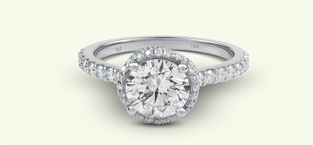 Vue de dessus d'une bague de fiançailles en diamant taille brillant avec un halo, montrant le poinçon 19KT gravé sur l'anneau.