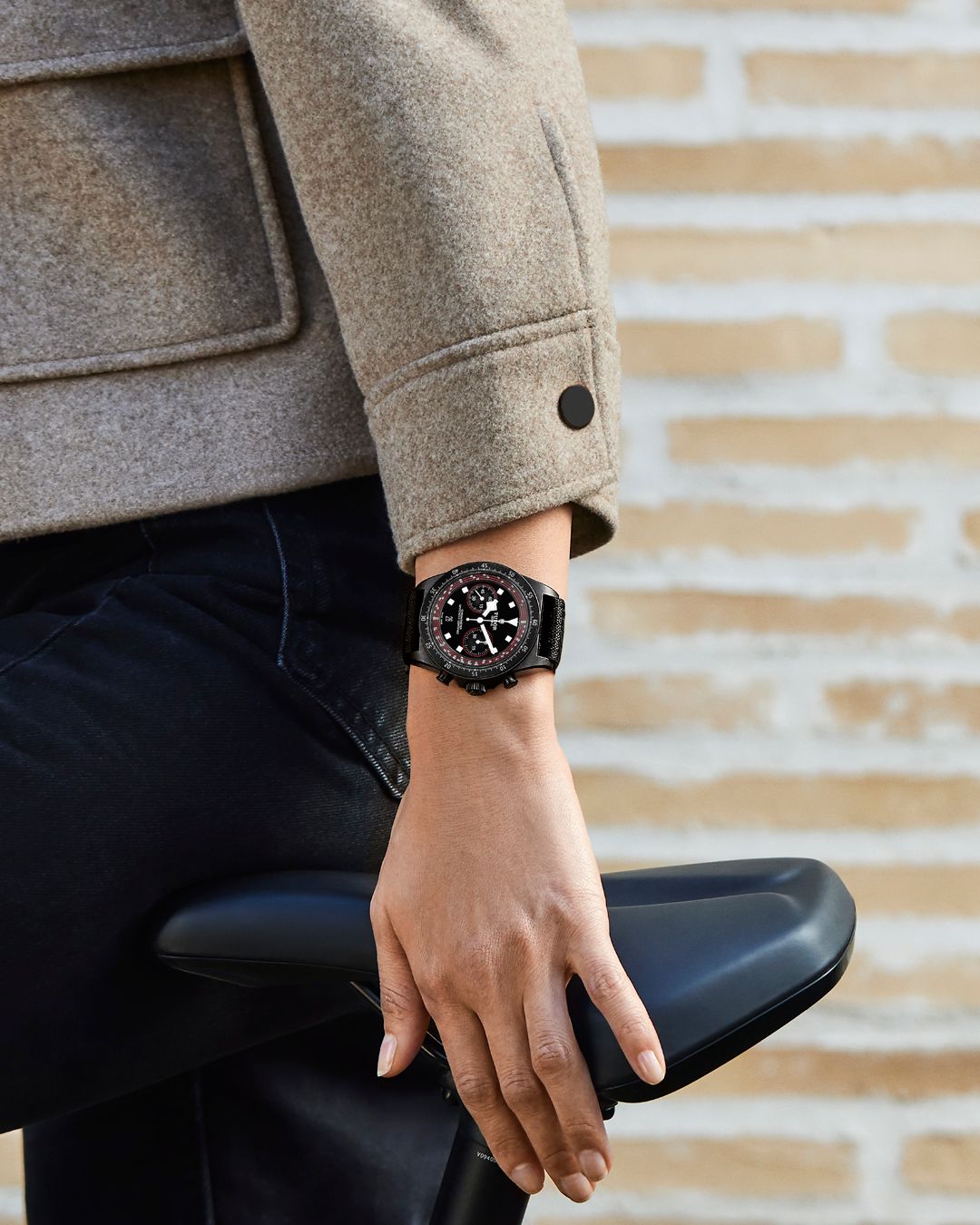 Gros plan sur une personne portant une montre de luxe Tudor noire tout en tenant une selle de vélo, alliant élégance et style sportif.