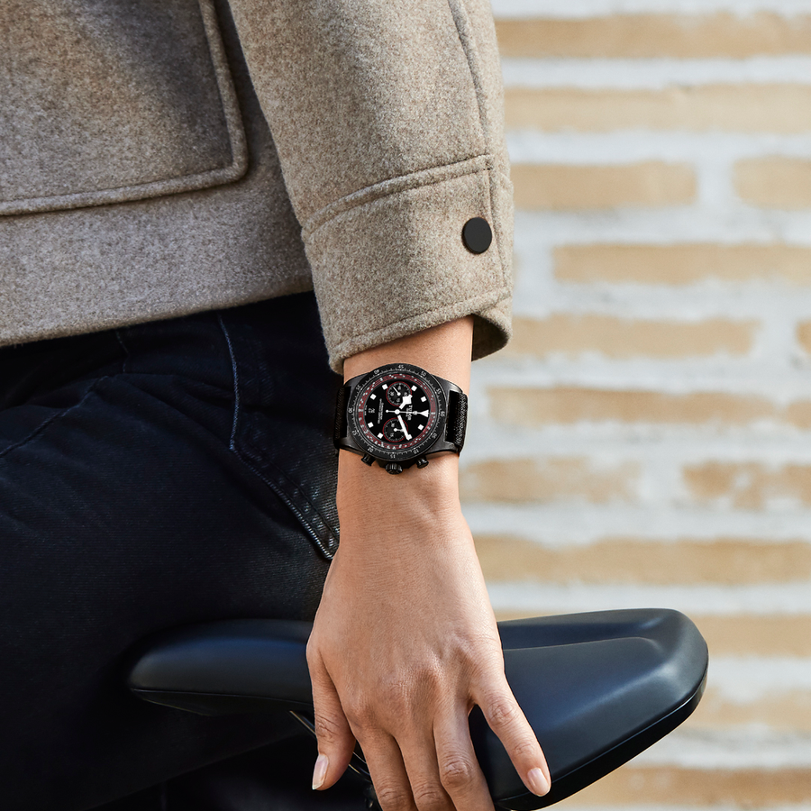 Gros plan sur une personne portant une montre de luxe Tudor noire tout en tenant une selle de vélo, alliant élégance et style sportif.