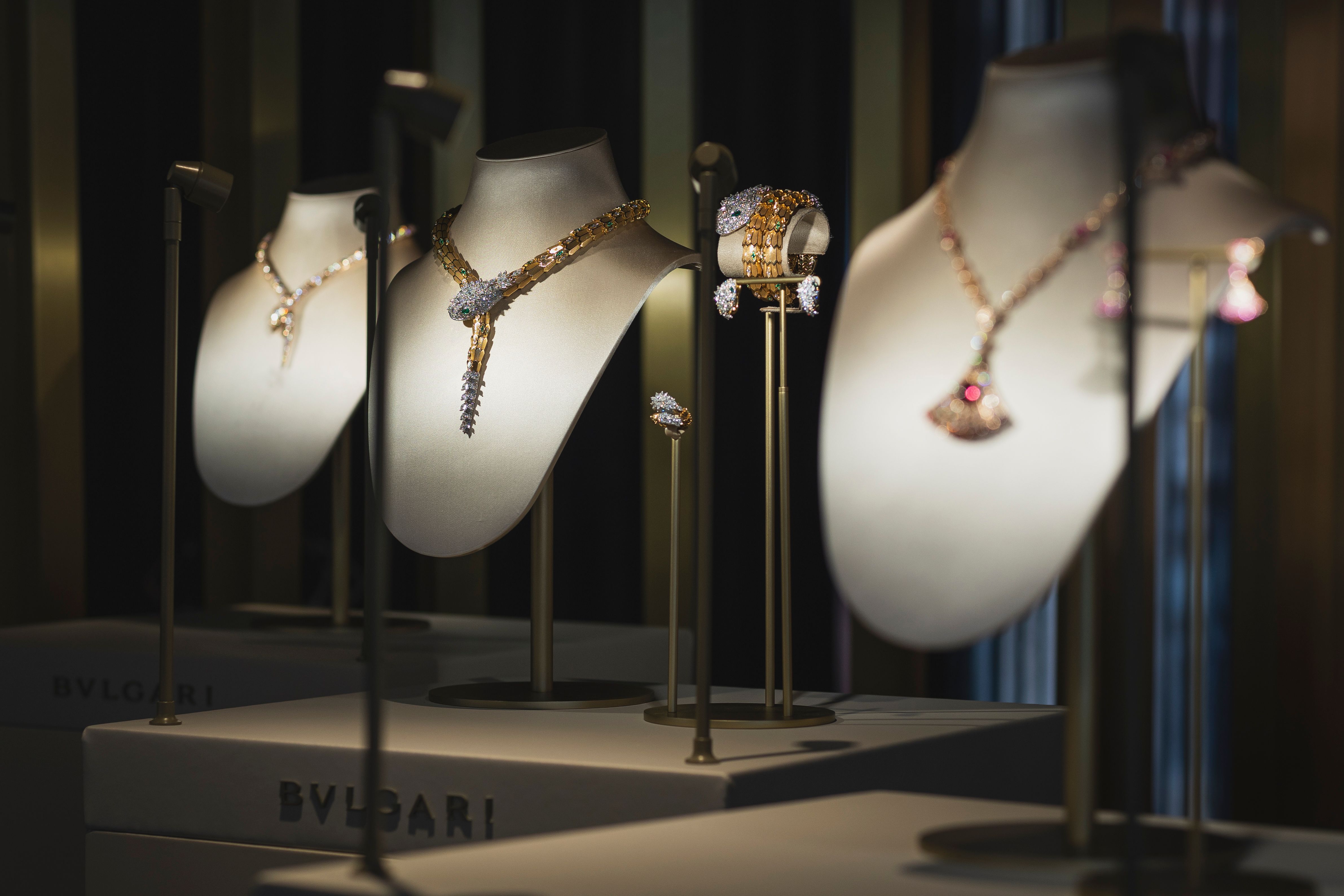 High jewelry display featuring dazzling Bulgari necklaces, rings, and bracelets, showcased on elegant busts under focused lighting.