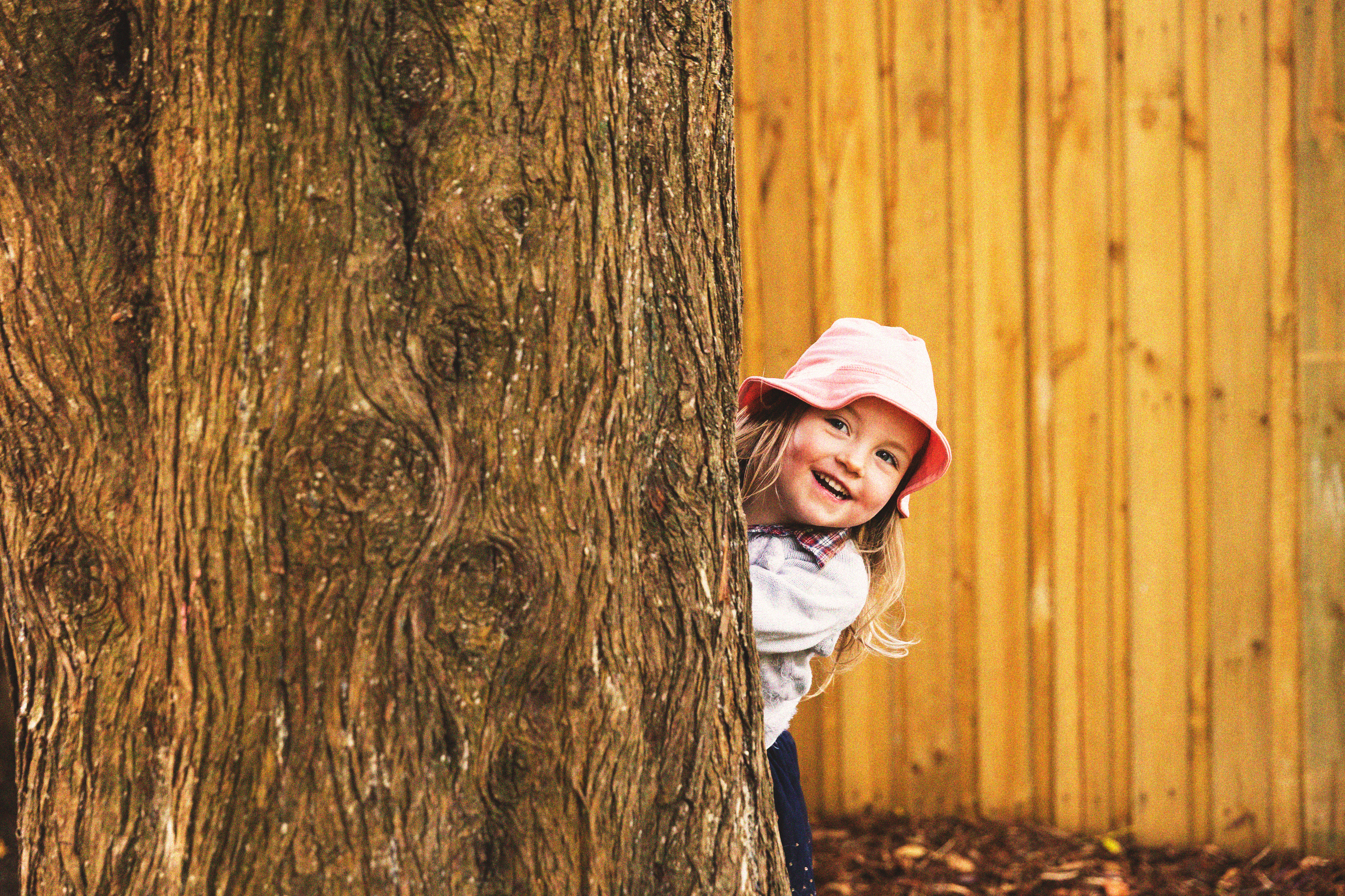A young girl leaning out from behind a tree