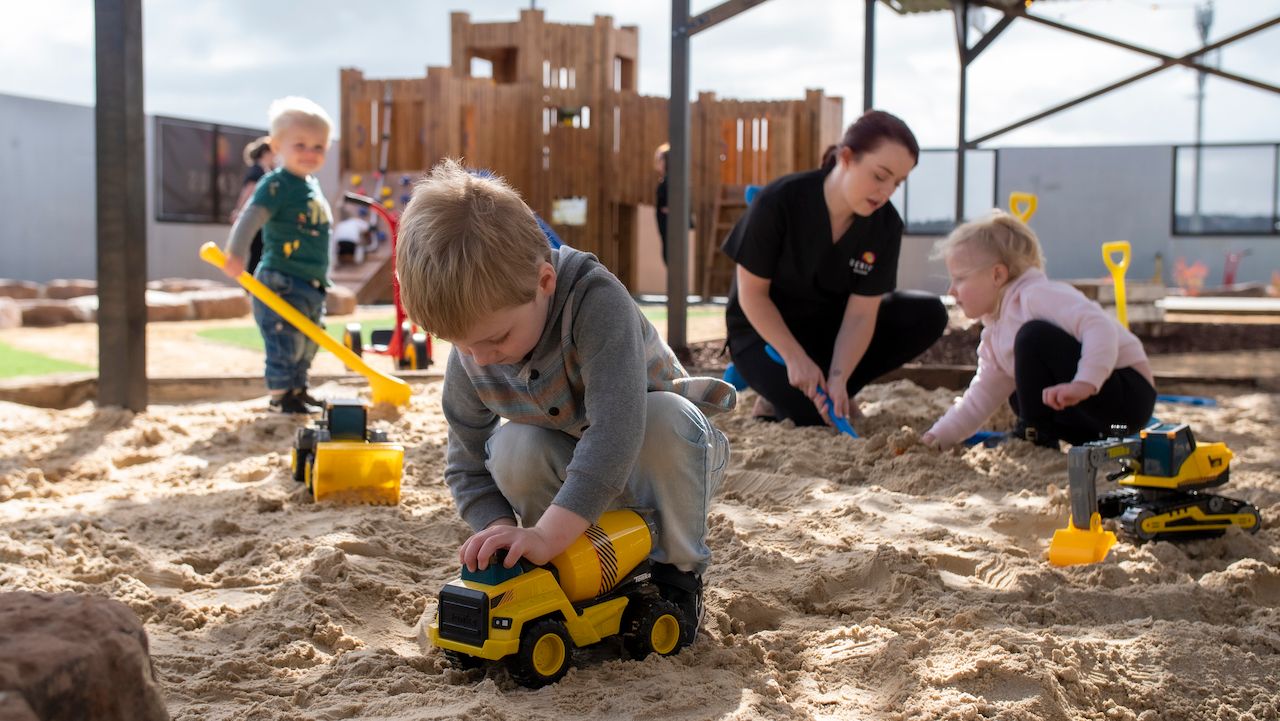 Young children and an educator play in a sandpit