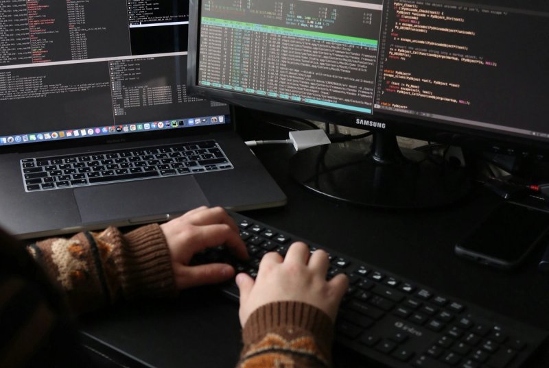 An image of a person typing on a computer keyboard. There computer code showing on the screen.