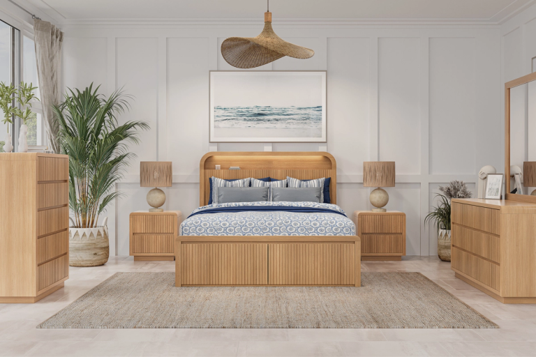 A modern light wood bedroom set featuring a slatted bed, nightstands, chest, and dresser with mirror, styled with blue bedding and coastal decor.