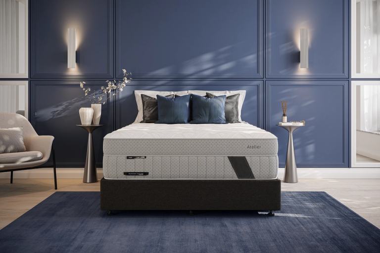 An Atelier grey and white mattress on a dark bed frame in a modern blue bedroom.