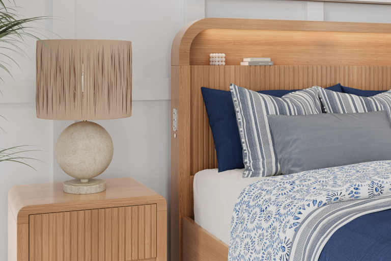 A modern bedroom with a light wood nightstand and textured lamp, next to a bed with blue and white patterned bedding and a fluted wooden headboard with integrated lighting.