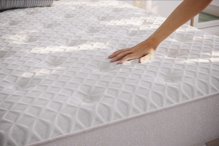 A hand presses down on a white, patterned mattress.