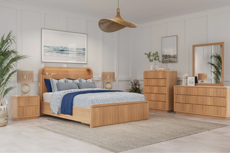 A bright bedroom with light wood furniture including a bed, two nightstands, a dresser with a mirror, and a chest of drawers, decorated in a coastal style.