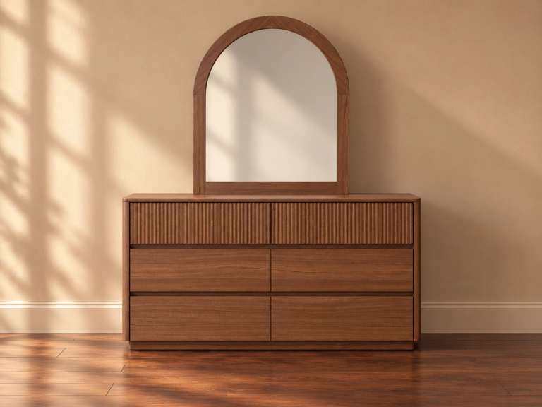 A wooden dresser with ribbed top drawers and an arched mirror, against a beige wall with sun shadows.