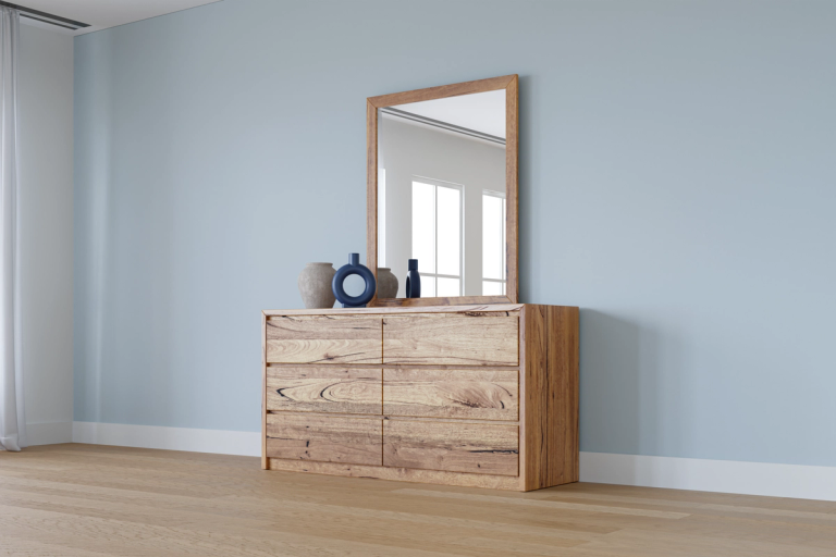 Natural wood dresser with six drawers and a mirror, topped with three decorative vases, in a room with light blue walls.
