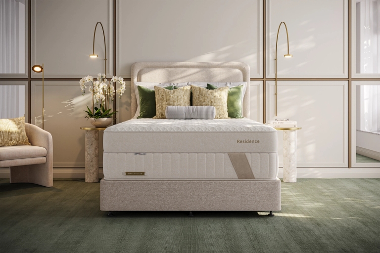 A luxurious bedroom with a light-colored bed featuring a "Residence" mattress, elegant decor, and warm lighting.