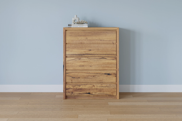 A four-drawer wooden chest of drawers against a light blue wall, with books and decor on top.