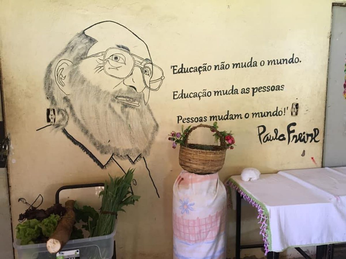 Photo above: Table, basket, plants at MST school in Brasil in front of a mural of Paulo Freire and his quote (translated), "Education does not change the world. Education changes people. People transform the world."