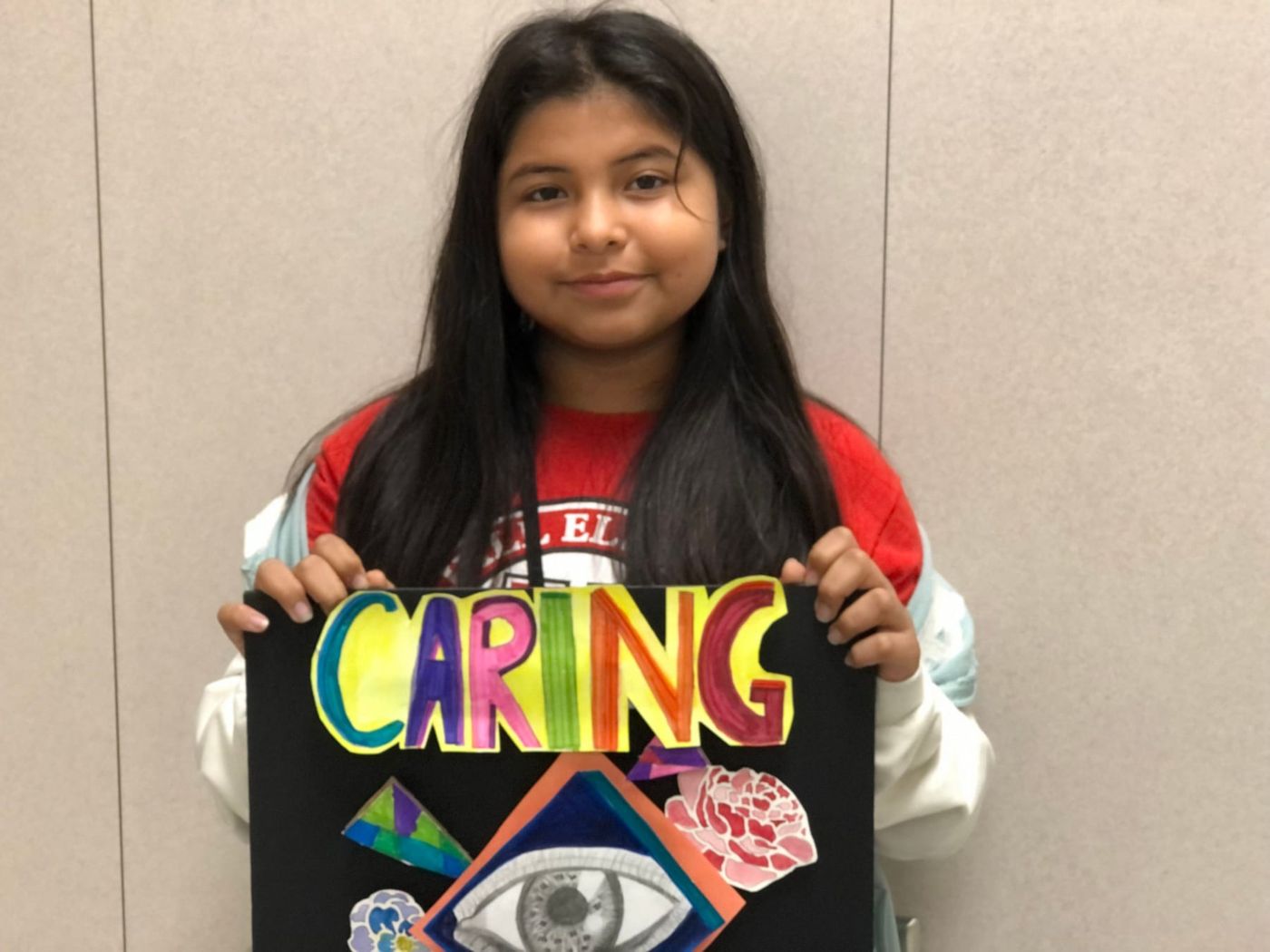 A student holding up a poster she made with the word Caring
