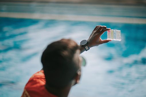 Un homme qui test l'eau de sa piscine avec un kit de test ph 