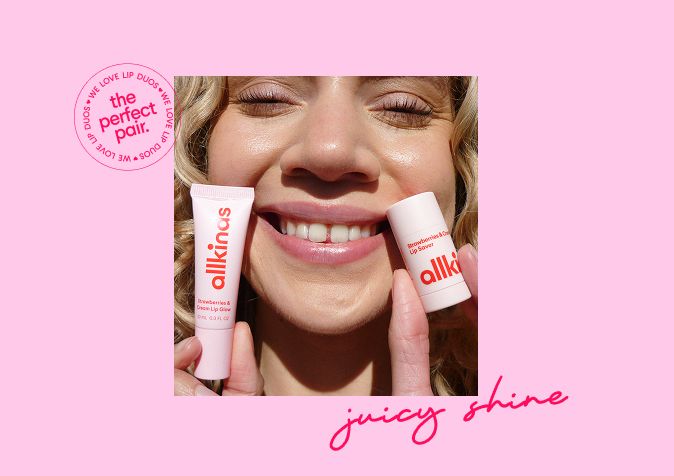 Smiling person with glossy lips holds a pink allkinos 'Strawberry & Cream Lip Glow' tube and 'Lip Saver' stick.