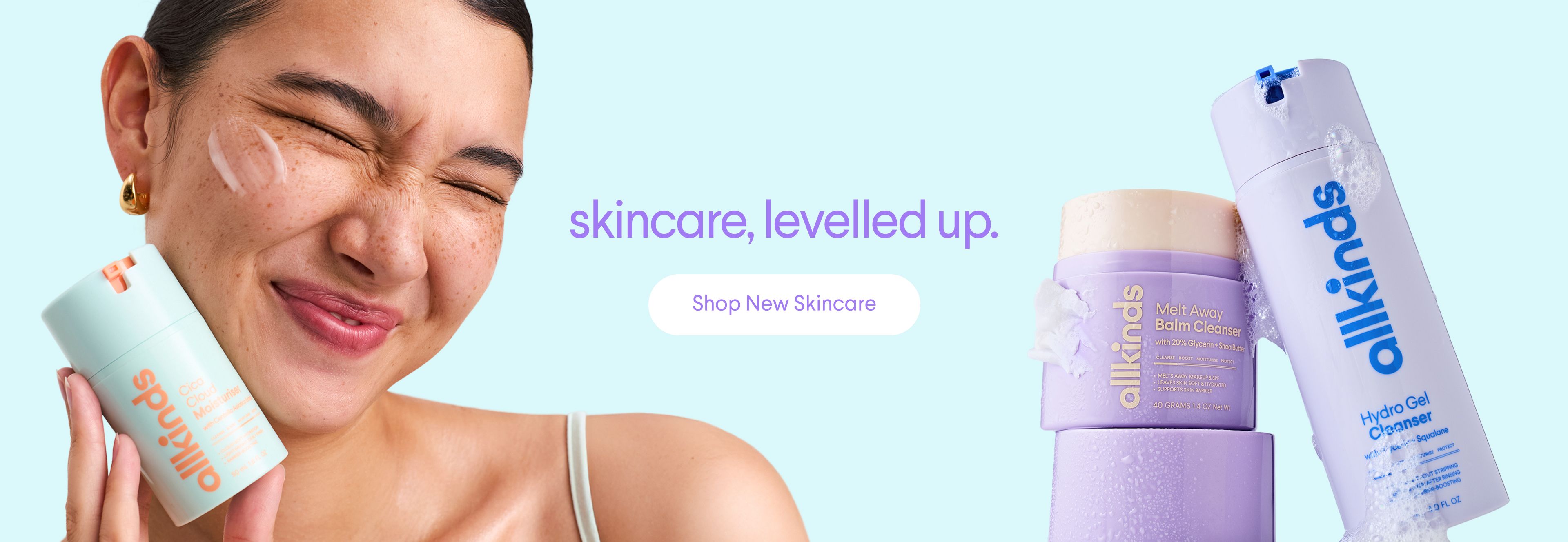 allkinds skincare ad: Smiling woman with cream on her face holds a light blue product tube. A purple jar and bottle of allkinds products are nearby. Text: 'skincare, levelled up.' and 'Shop New Skincare'.