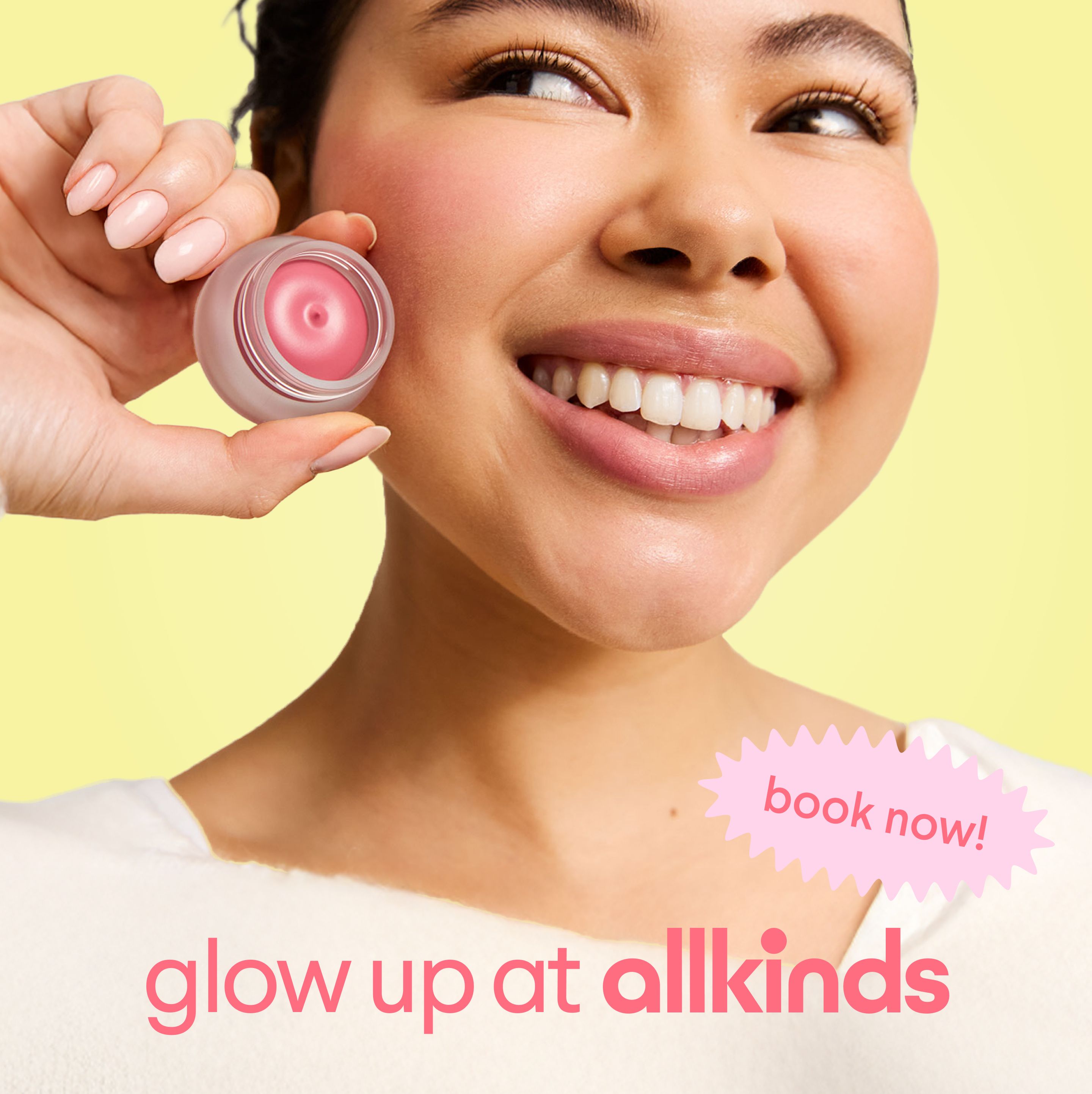 a woman is smiling while holding a blush in front of her face .