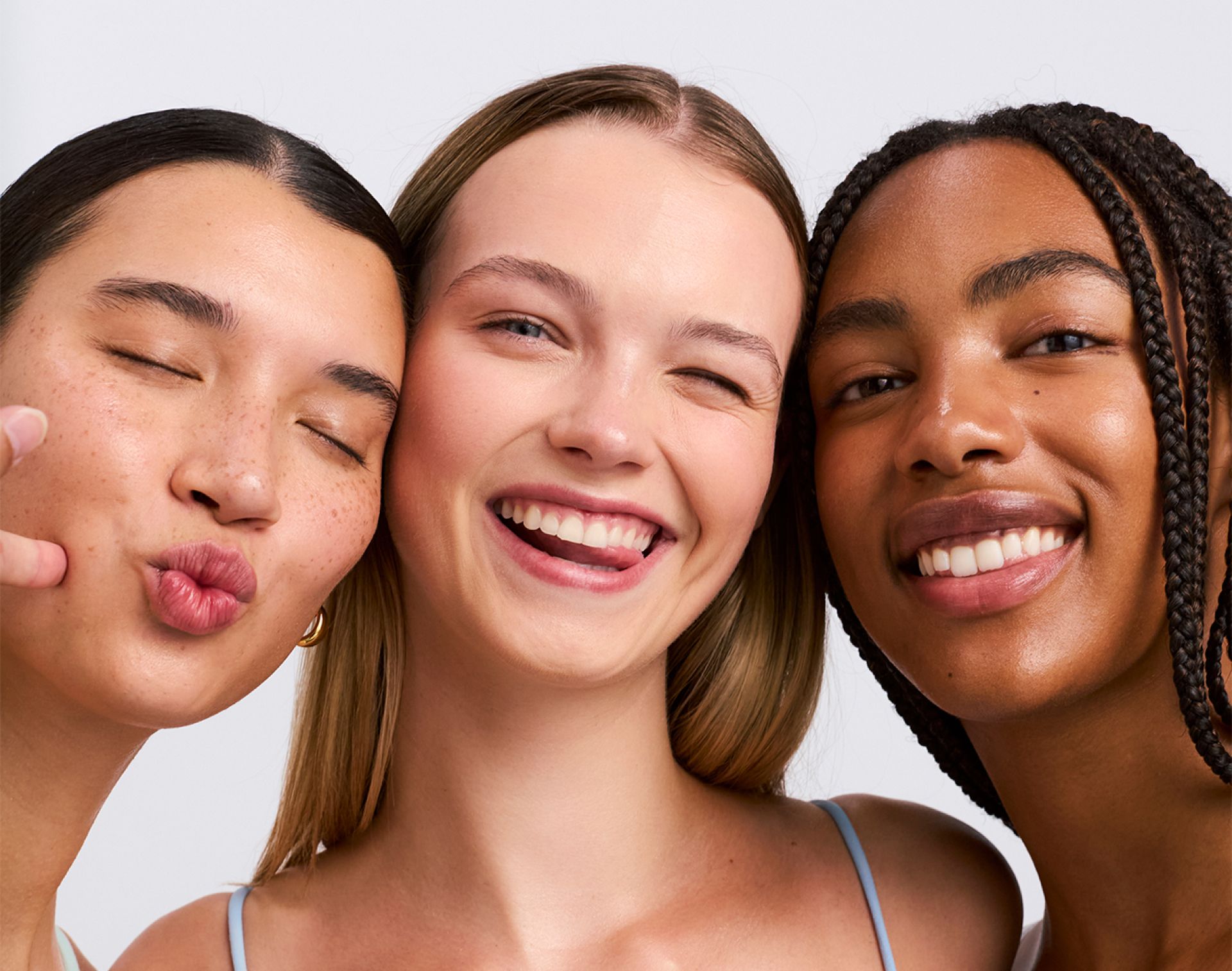 Three smiling young women with diverse skin tones making playful faces.