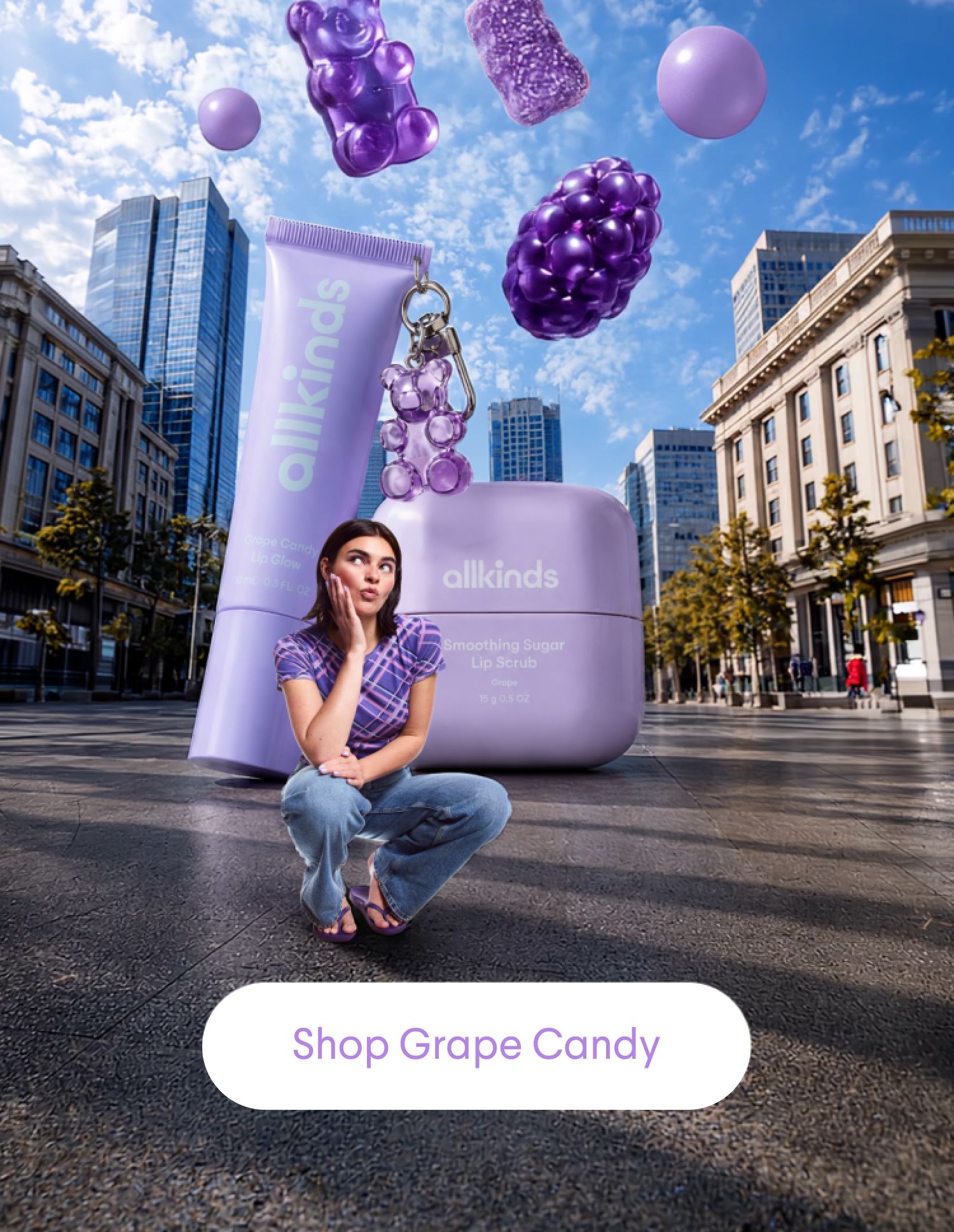 A woman crouches next to giant Allkinds lavender lip products in a city, with floating purple candies and a 'Shop Grape Candy' button.
