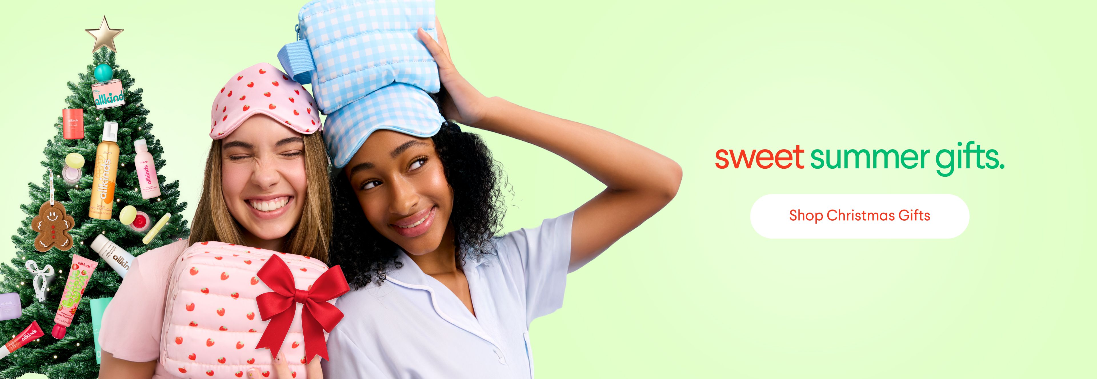 Two smiling women in sleep masks and pajamas pose with a gift and a Christmas tree decorated with beauty products; text reads 'sweet summer gifts.' and 'Shop Christmas Gifts'.