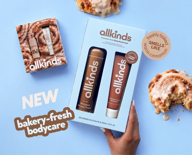 A hand holds an "allkinds" brand "Cinnamon Scroll Body Routine Set" box, next to a smaller "allkinds" box and two iced cinnamon rolls. Text overlays read "NEW bakery-fresh bodycare" and "SMELLS LIKE warm cinnamon."