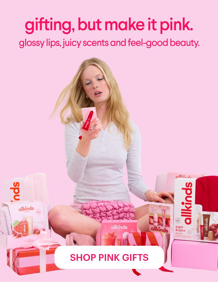 A woman sits on a pink floor surrounded by pink "allkinds" beauty gifts and products, holding one item. Overlay text reads "gifting, but make it pink." and "SHOP PINK GIFTS."