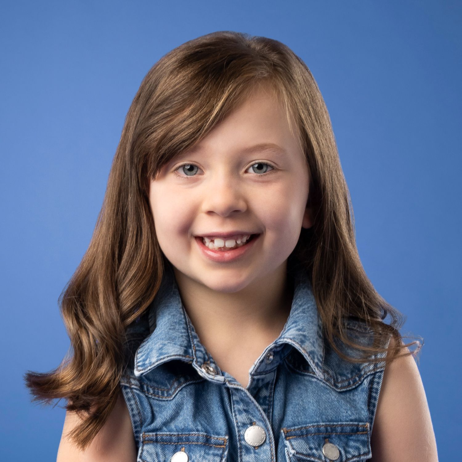 a young girl is wearing a denim vest and smiling for the camera .