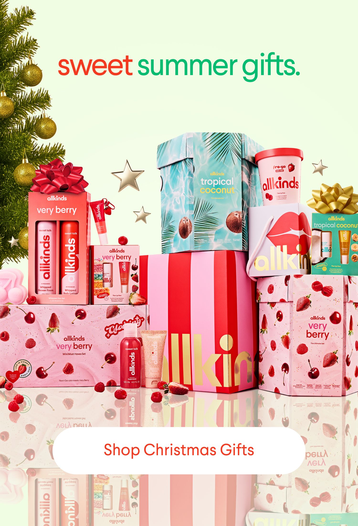 A colorful display of allkinds brand "very berry" and "tropical coconut" gift sets, with a Christmas tree and stars. Text: "sweet summer gifts. Shop Christmas Gifts."