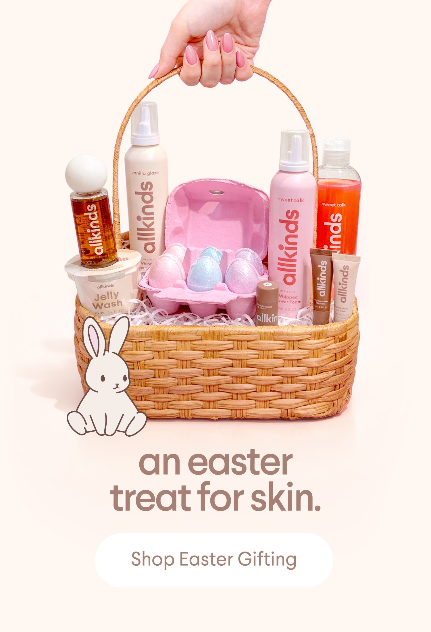 An Easter basket brimming with allkinds skincare products and pastel egg-shaped bath bombs, next to a cartoon bunny.