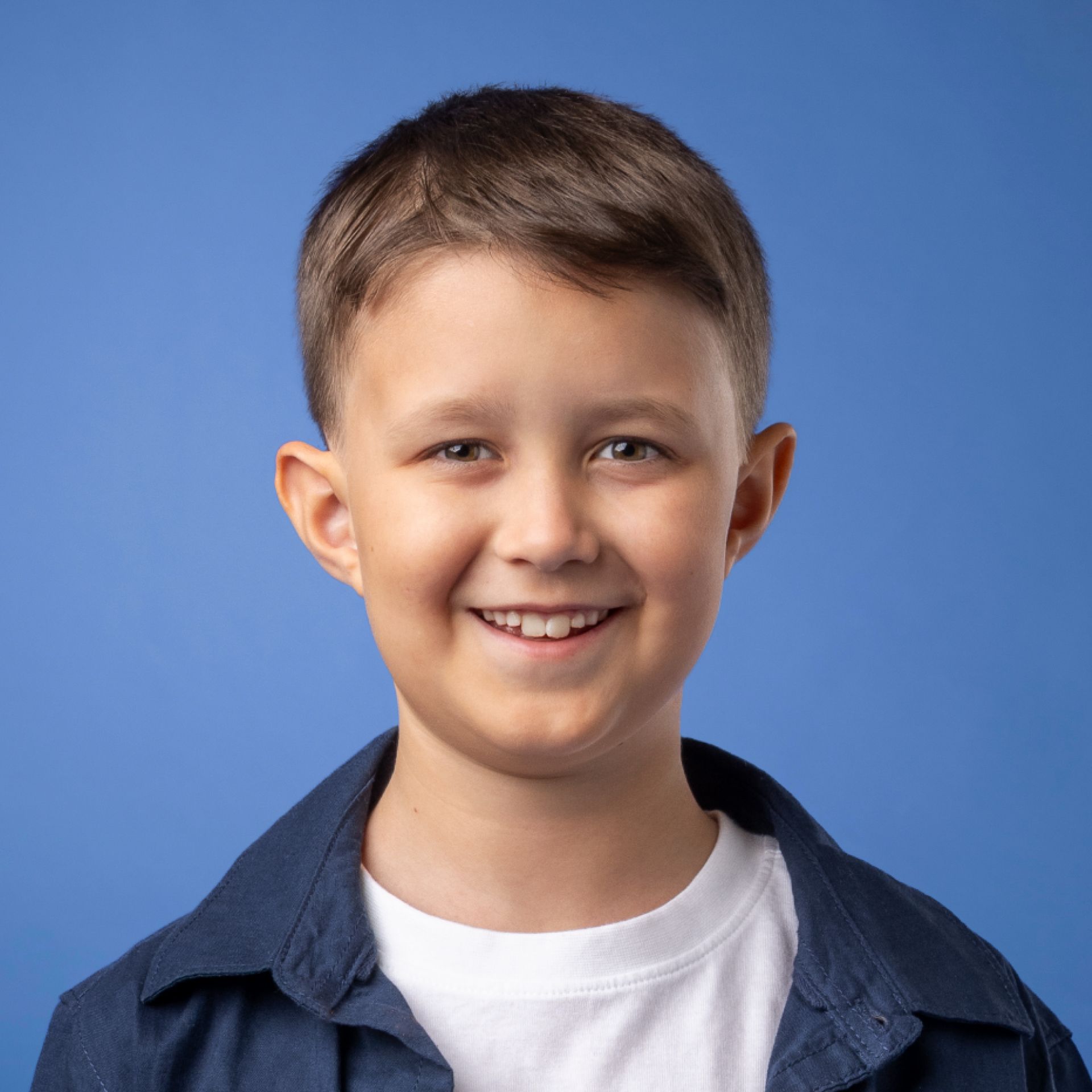 a young boy in a blue shirt and white shirt is smiling for the camera .